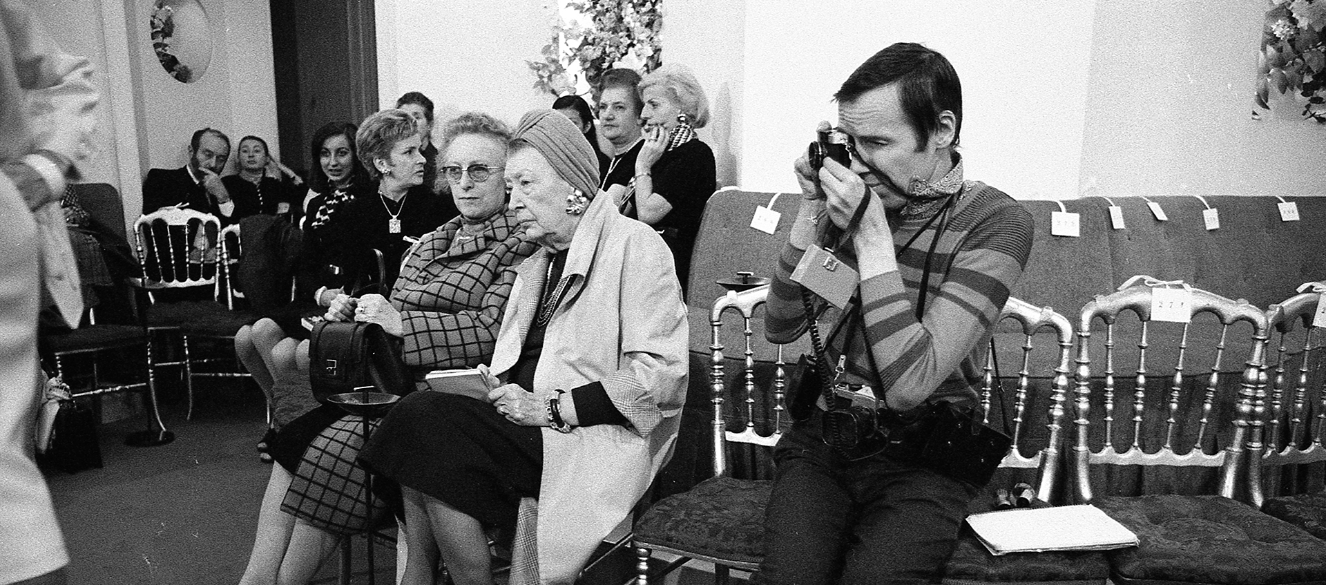 Photographer Bill Cunningham taking a shot seated among onlookers in Paris 1971.