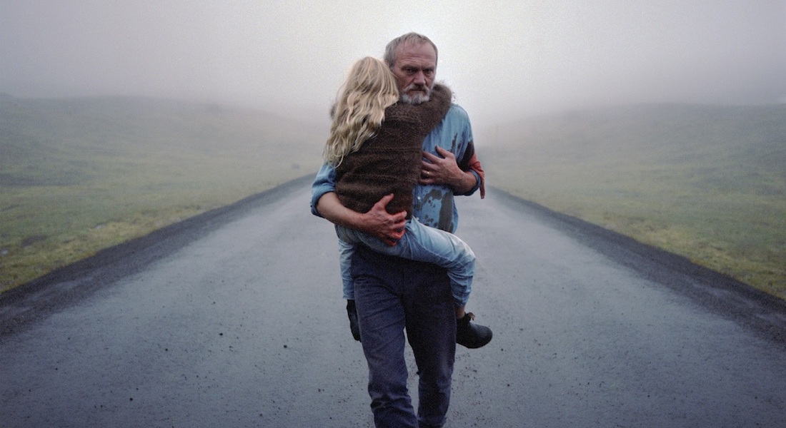 A man holds his young child in his arms as he walks down an empty country road in a scene from the Icelandic drama A White, White Day