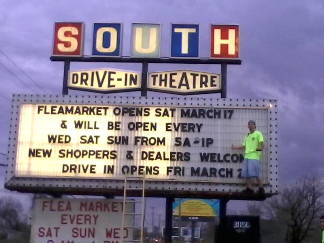 A worker at South Drive-In in Columbus, Ohio stands on the ledge of the theater's lit marquee