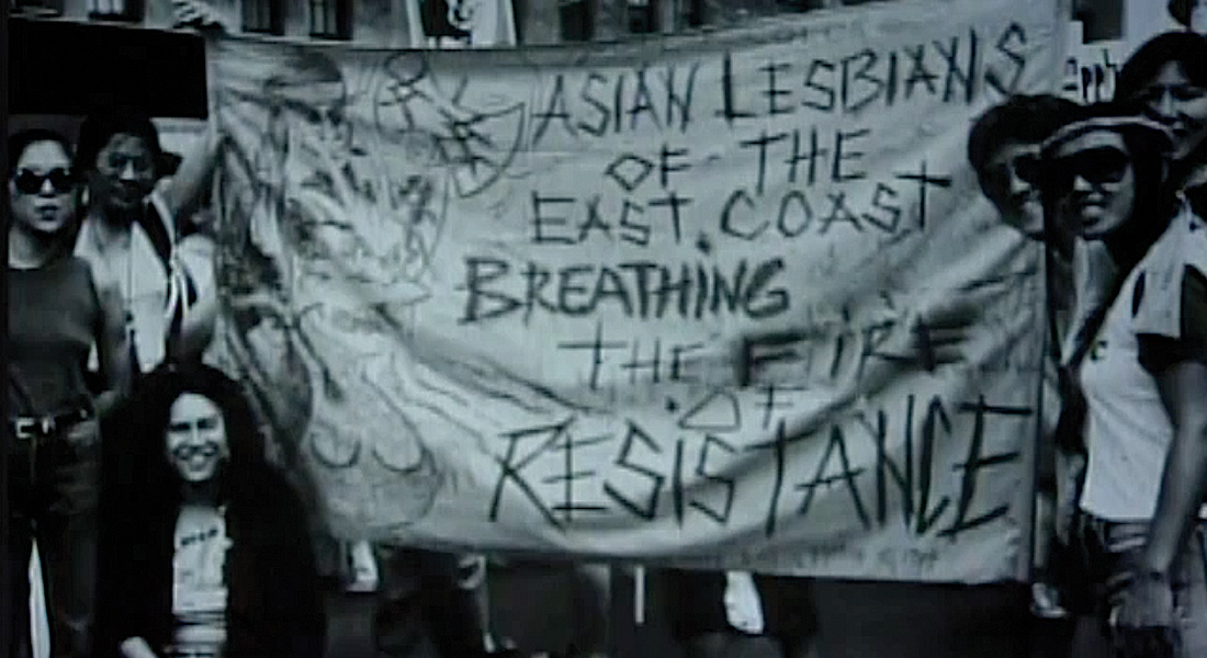 A group of women hold up a fabric banner that reads "Asian lesbians of the East Coast breathing the fire of resistance"