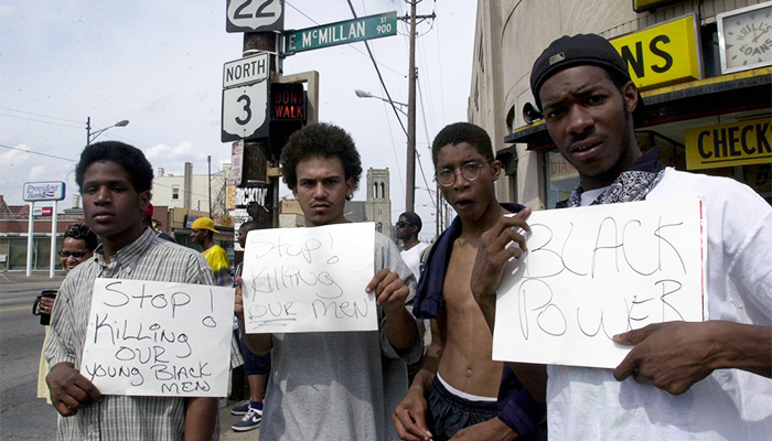 Four Black men hold signs protesting the killing of young black men.