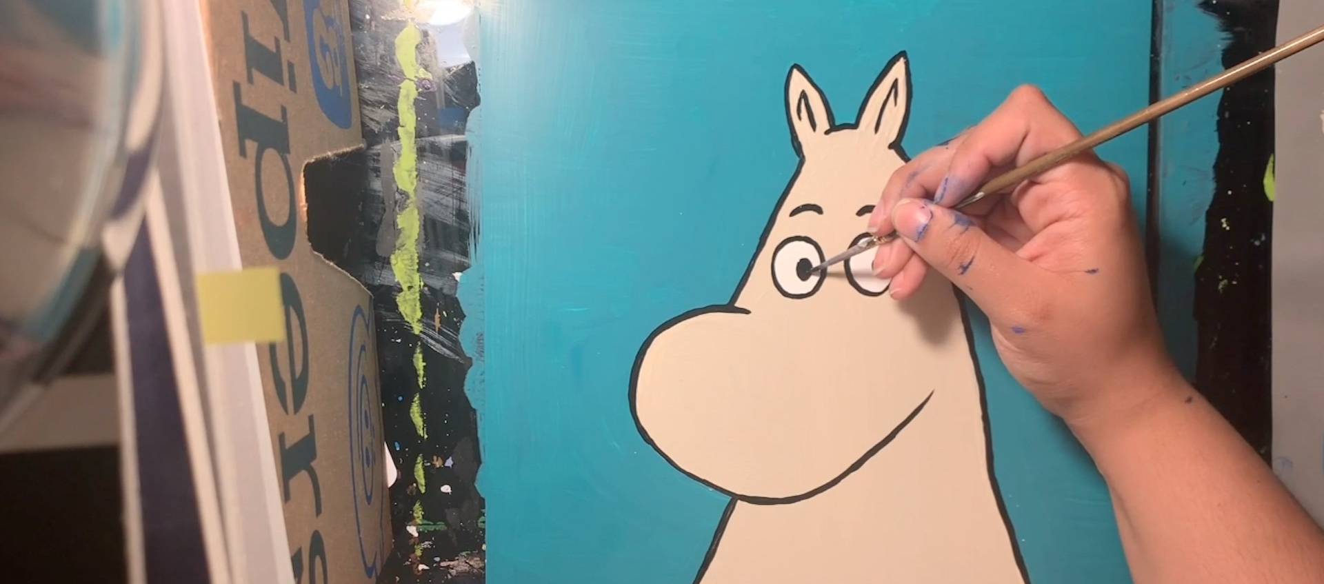 The hand of artist Bethani Blake paints a Moomin figure