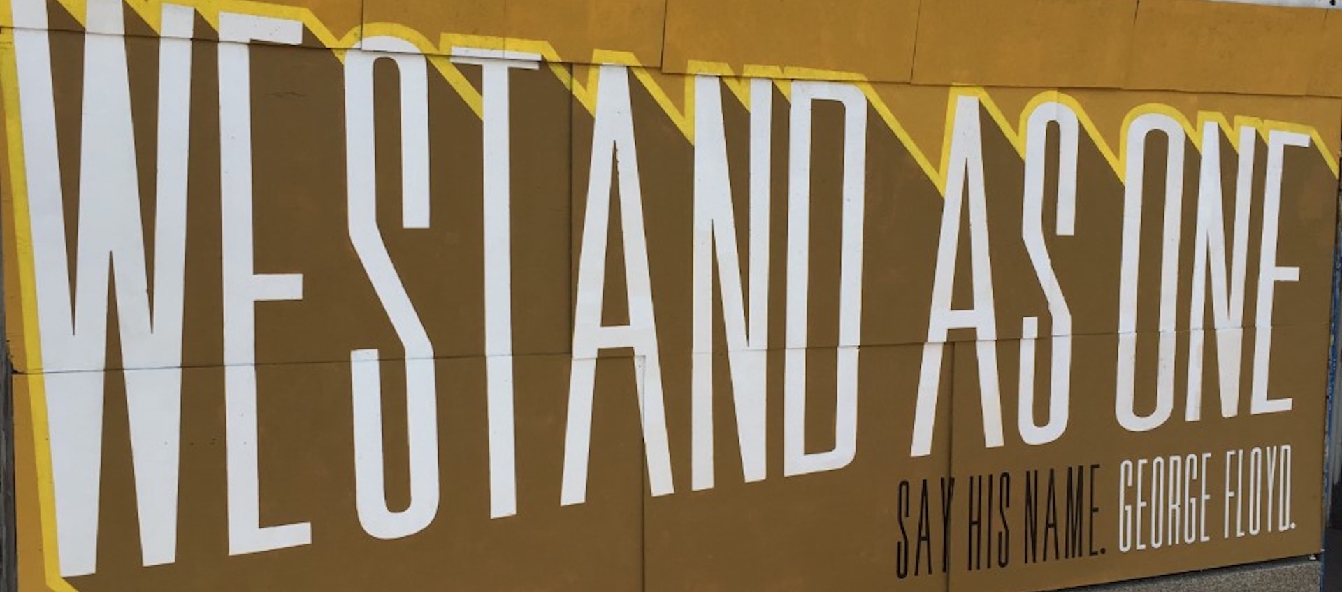 A mural that reads "we stand as one" painted on boards used to cover front windows of a pawn shop during the Columbus George Floyd protests in June 2020. Mural organized by Flat Black Commercial Visuals