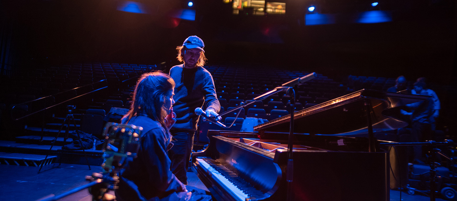 Erin Durant sits at a piano on stage as a crew person places a mic in front of her
