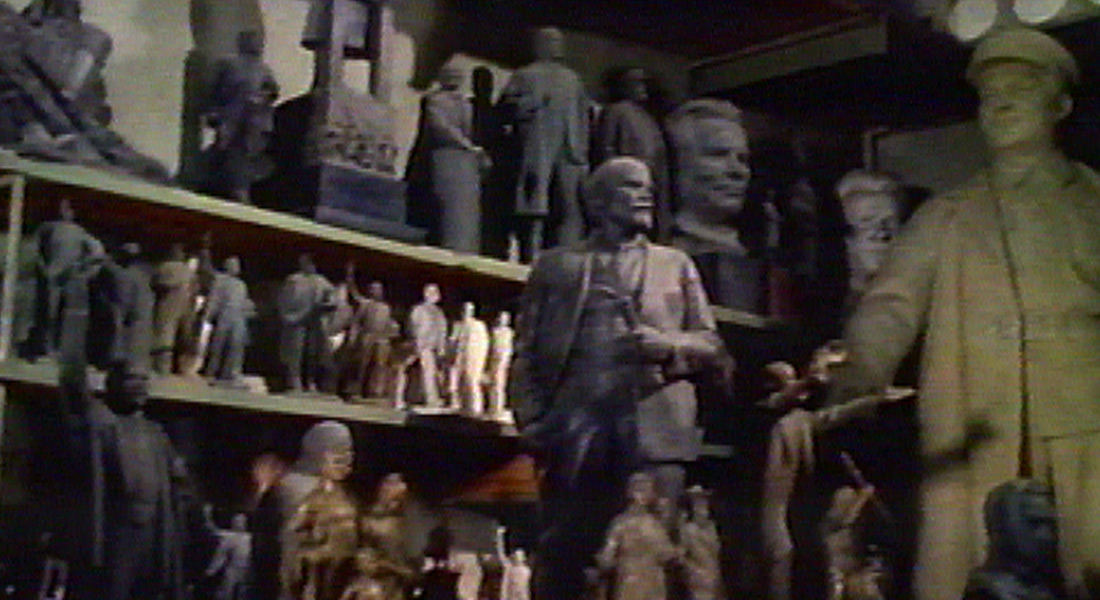 A warehouse full of old Soviet monuments, with a statue of Lenin at the center of the shot