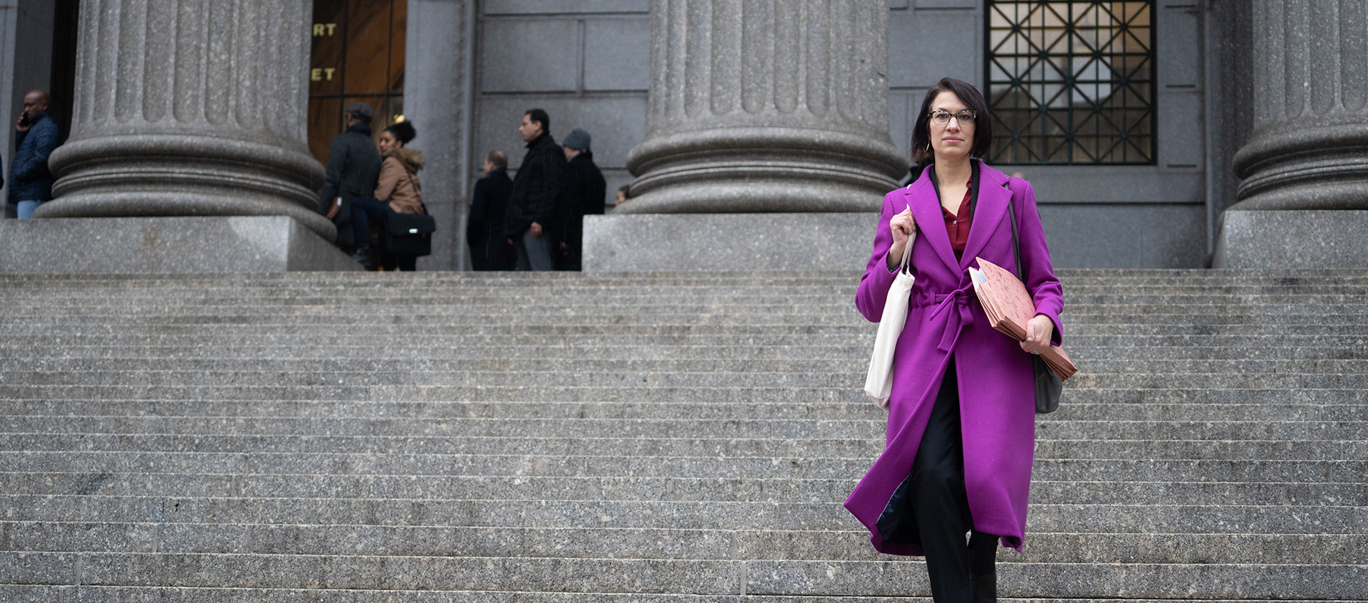 ACLU lawyer Brigitte Amiri descends a court staircase with files in hand wearing a purple coat