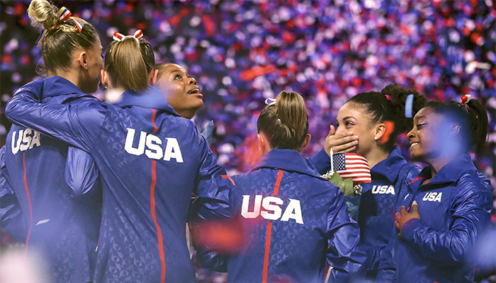 USA women's gymnastics team smiling and holding each other in celebration of victory