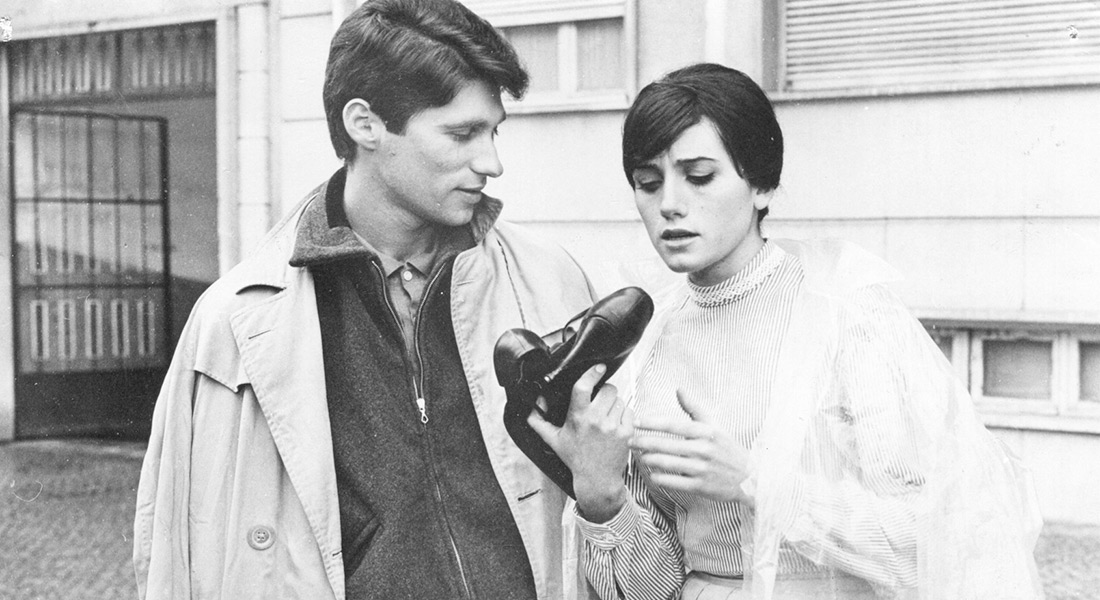 A black-and-white still of the film's young couple Julio and Ilda, with the latter examining a pair of shoes
