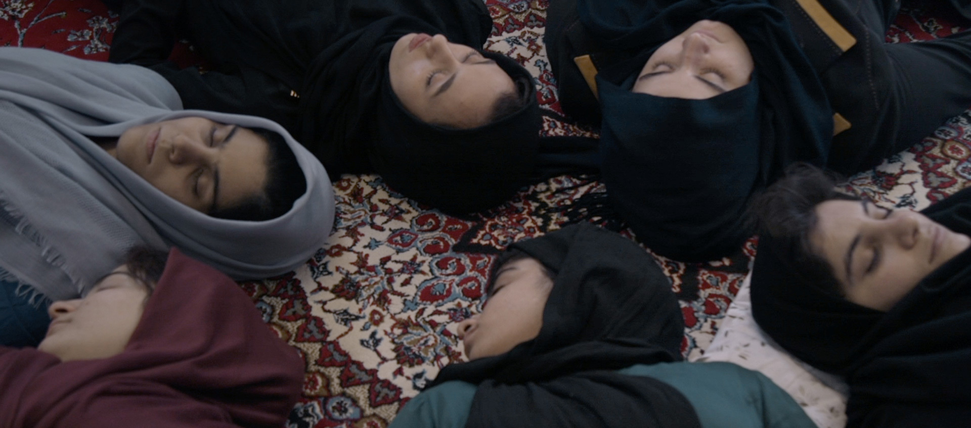A view of six women in hijabs lying with eyes closed on a carpet