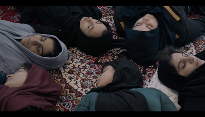 A view of six women in hijabs lying with eyes closed on a carpet
