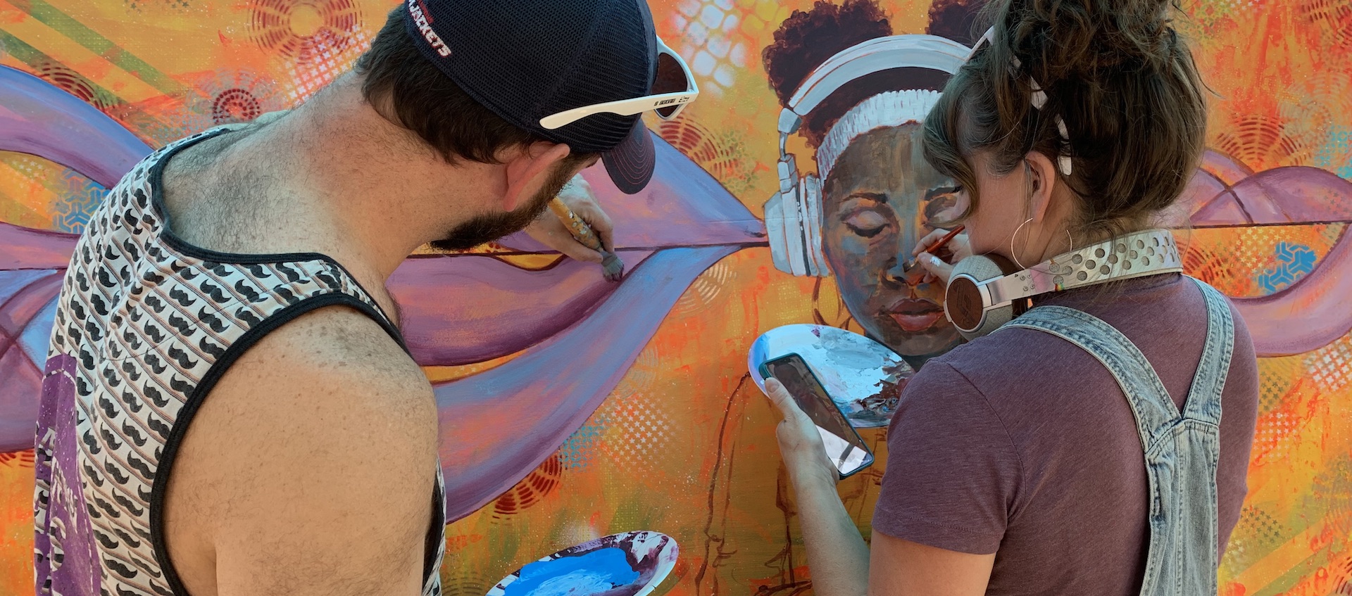 Artists Eric Rausch and Jen Kiko Rausch seen from behind as they work on a large scale painting during the 2019 Urban Scrawl event in Franklinton