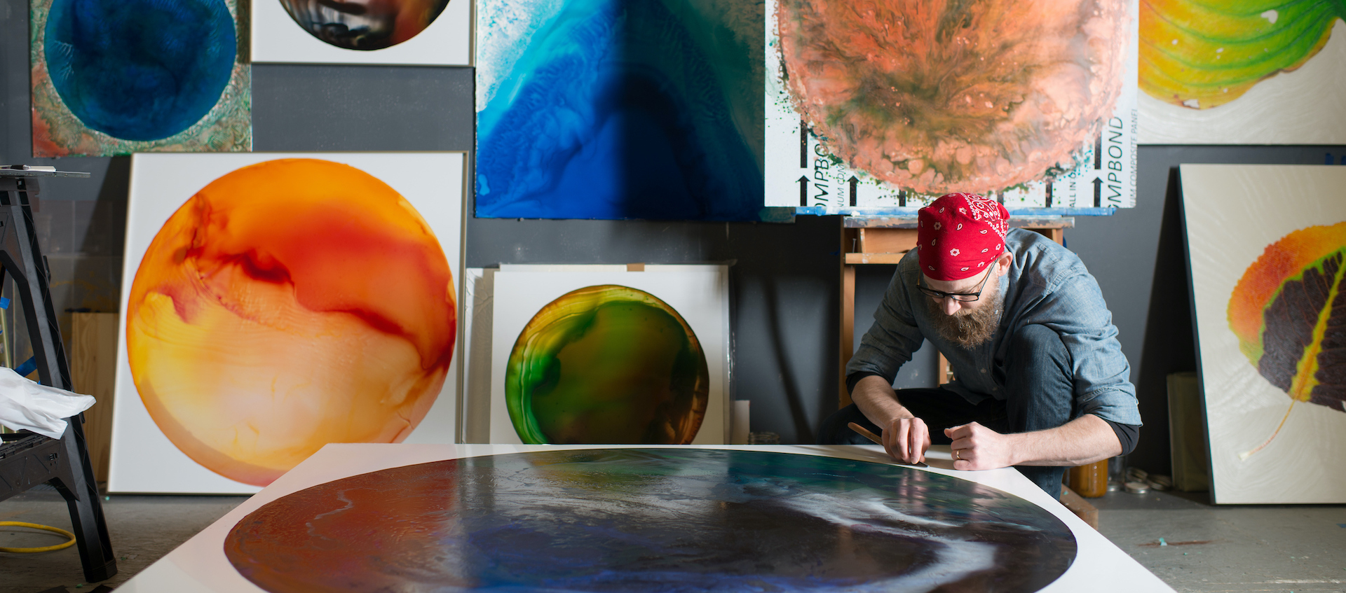 Artist John Sabraw works on a flat canvas with a circular abstract image, with other works in the same series hanging on the wall behind him