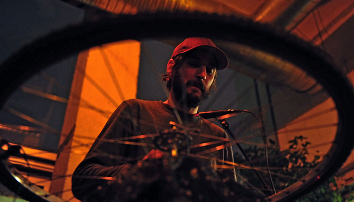 Rob Frye in hat performing, viewed through a spoked bicycle wheel