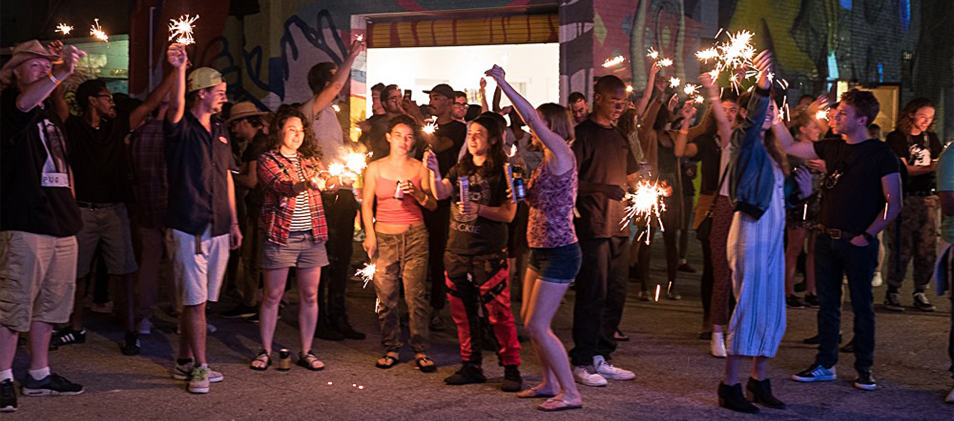 A nighttime scene of a crowd waving sparklers outside an entrance to 934 Gallery in Columbus