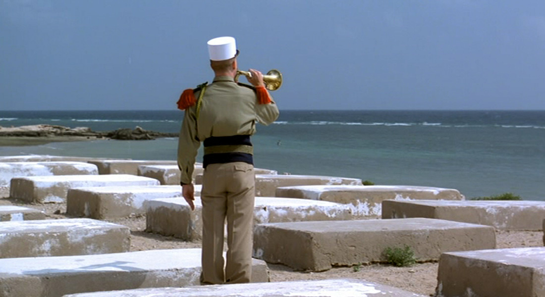 A soldier in uniform plays a bugle in front of the sea