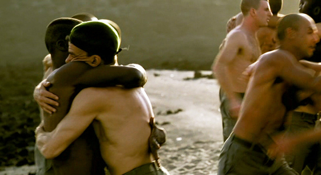 Several shirtless men embrace in a creek