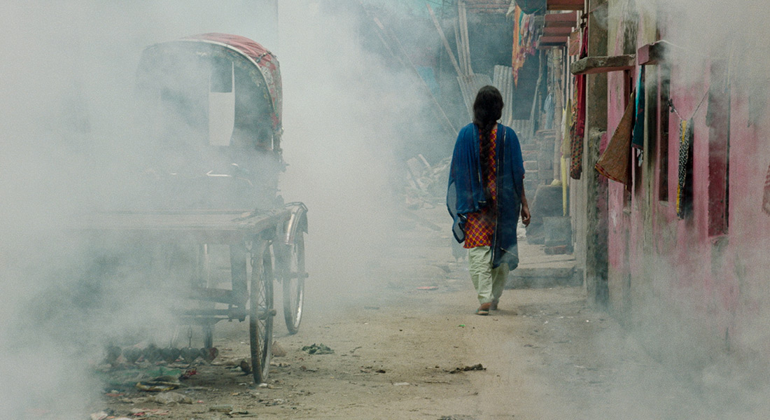 A woman walks away from the camera down a smoky street