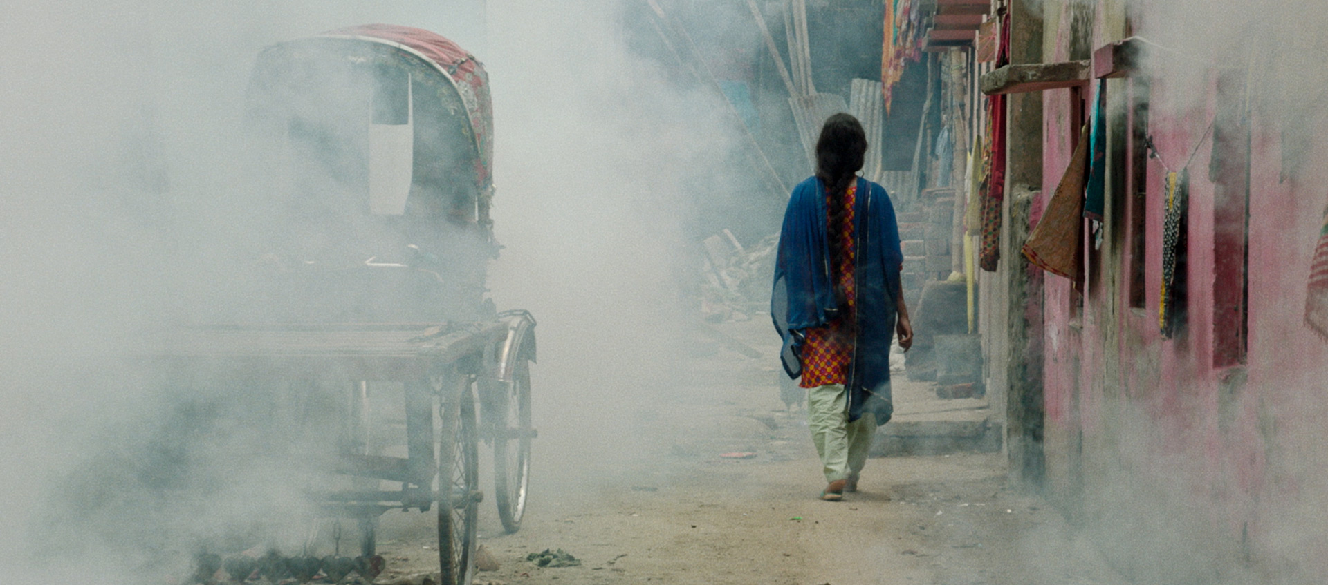 A woman walks away from the camera down a smoky street