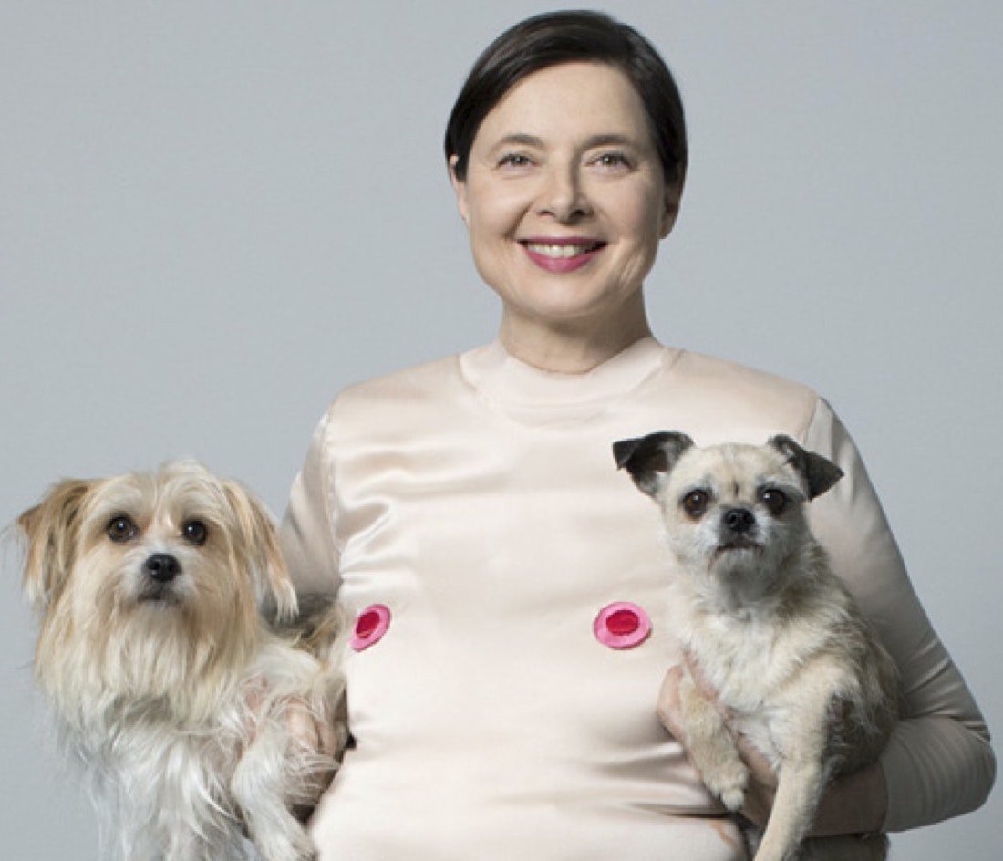 Actress-artist Isabella Rossellini wearing a light flesh-colored sleeveless bodysuit with appliqued nipples, holding a small dog under each arm