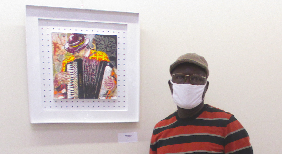 Wexner Center for the arts security guard Sam Adebuga stands wearing a face mask next to one of his paintings on view at John Glenn International Airport