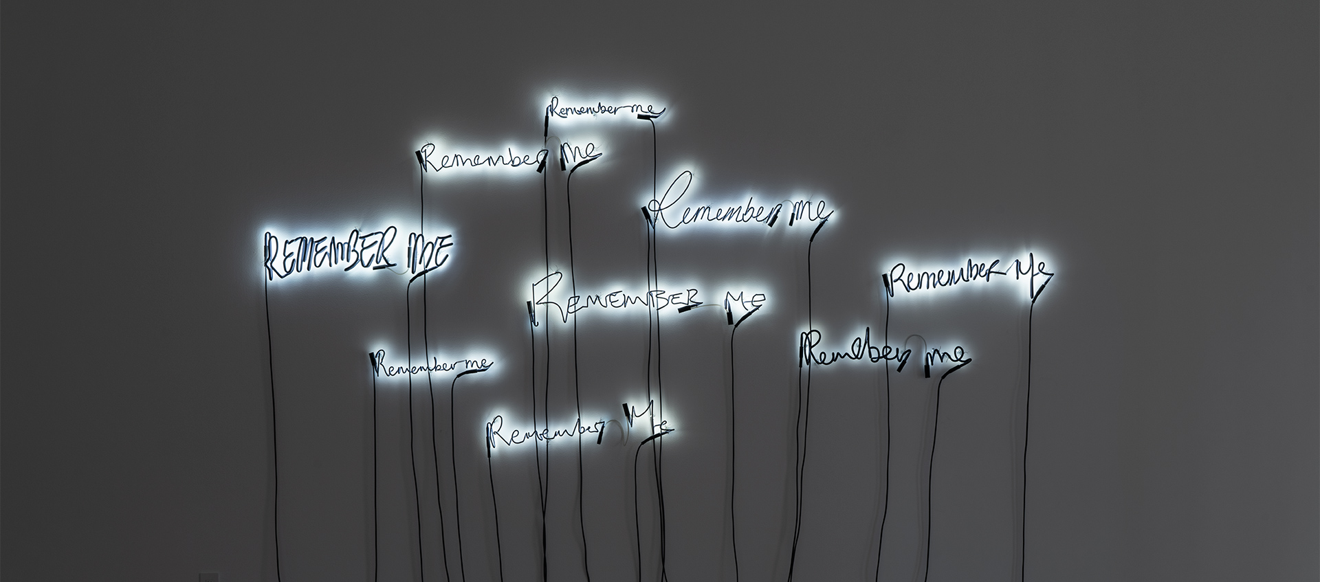 The words "Remember Me" are sculpted in neon and lit against a white wall.