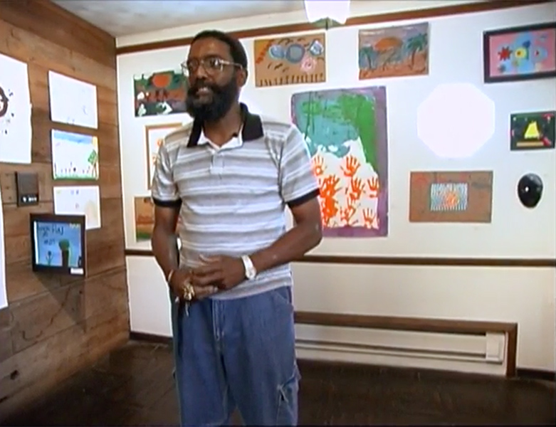 A man stands in front of wall with a selection of paintings on it