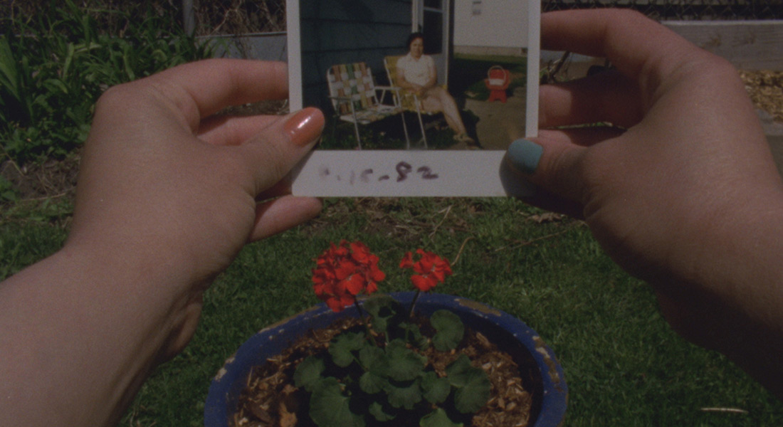 A close up of a hand holding a color Polaroid of a woman in folding chair dated 8-15-82