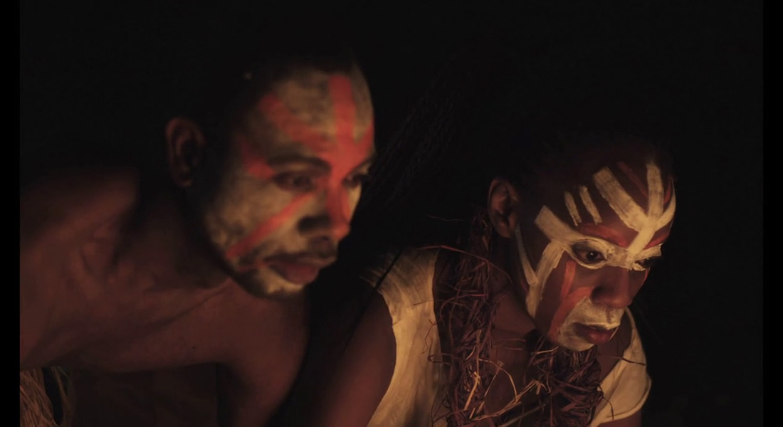 A man and woman in face paint look down at a source of light
