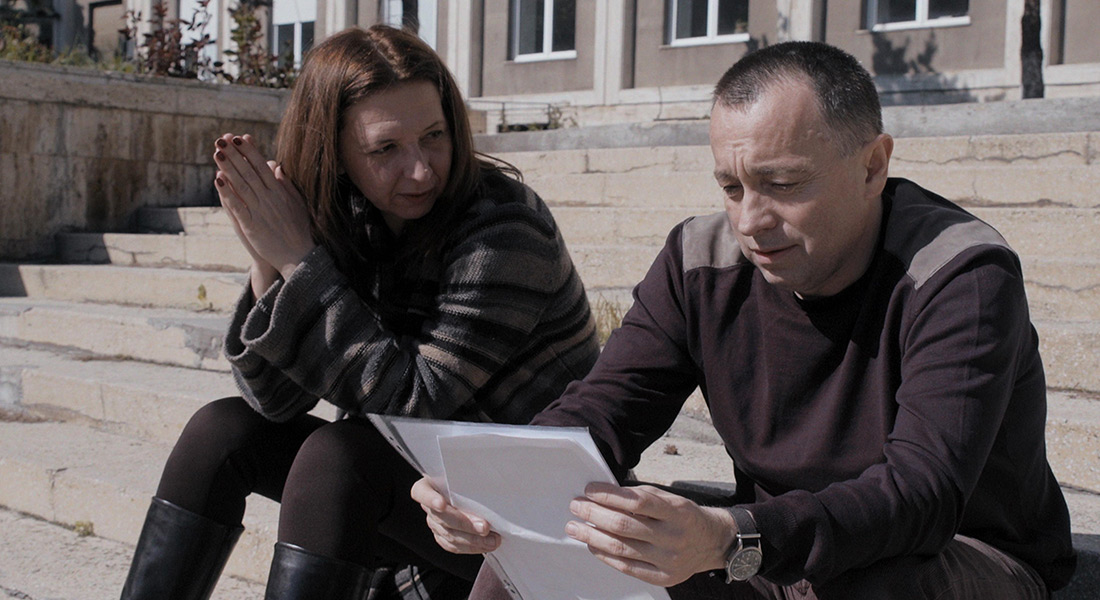 A woman, on the left, and a man, on the right, sit on steps reading a file