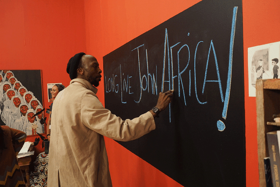 A man writes "Long live John Africa!" on a chalkboard.