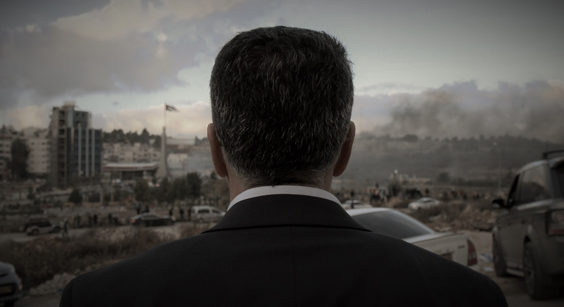 A man in a suit, seen from behind and from the shoulders up, looks out over a hazy city landscape.  