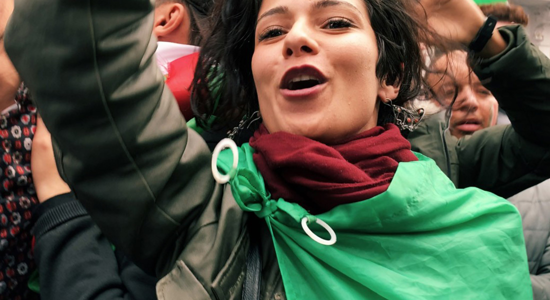 Close-up of a woman at a protest wearing the Algerian flag around her shoulders.