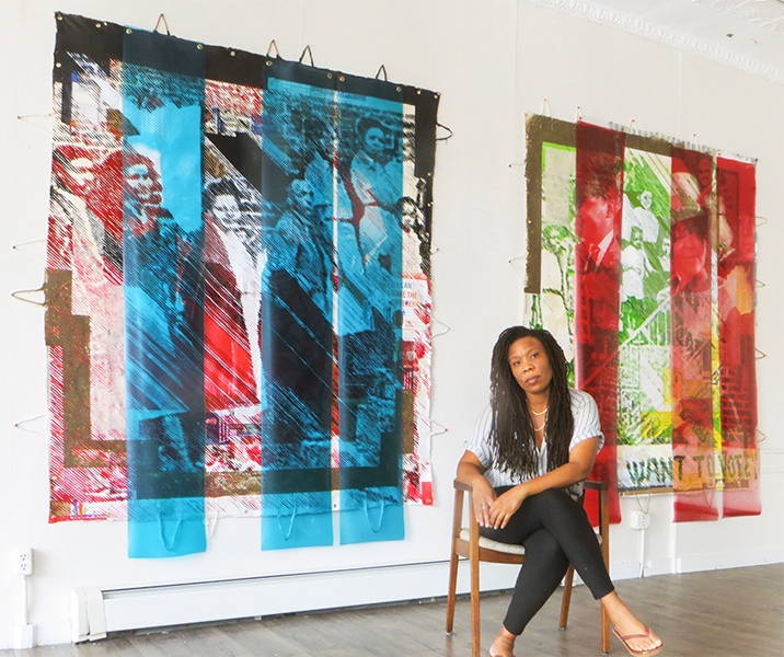Artist Tomashi Jackson is seated in front of two of her collage paintings