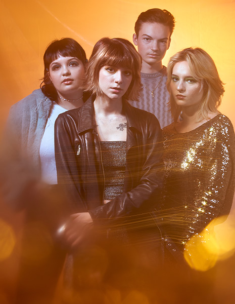 Four members of the band snarls standing in front of orangish yellow background