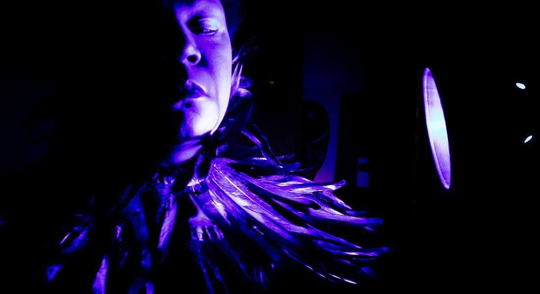 Image of a Sonic Arts Ensemble member bathed in purple light standing next to a small spotlight