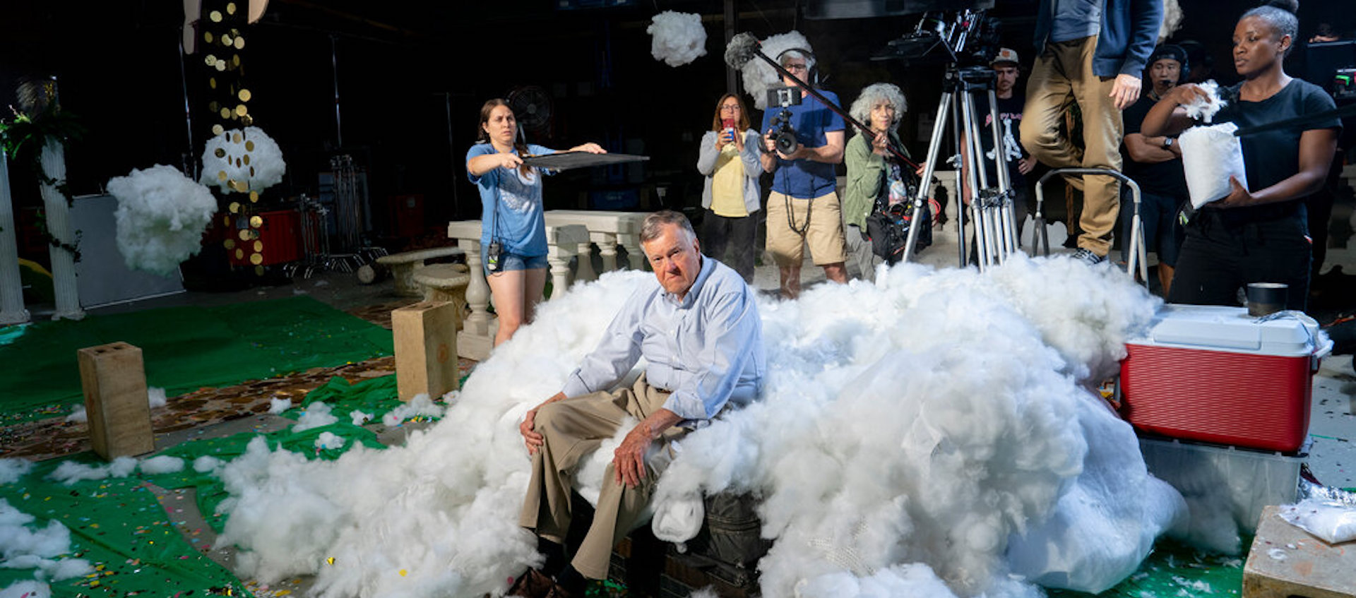 An elderly man sits in a pile of white fluff, surrounded by a camera crew, filming the documentary Dick Johnson is Dead