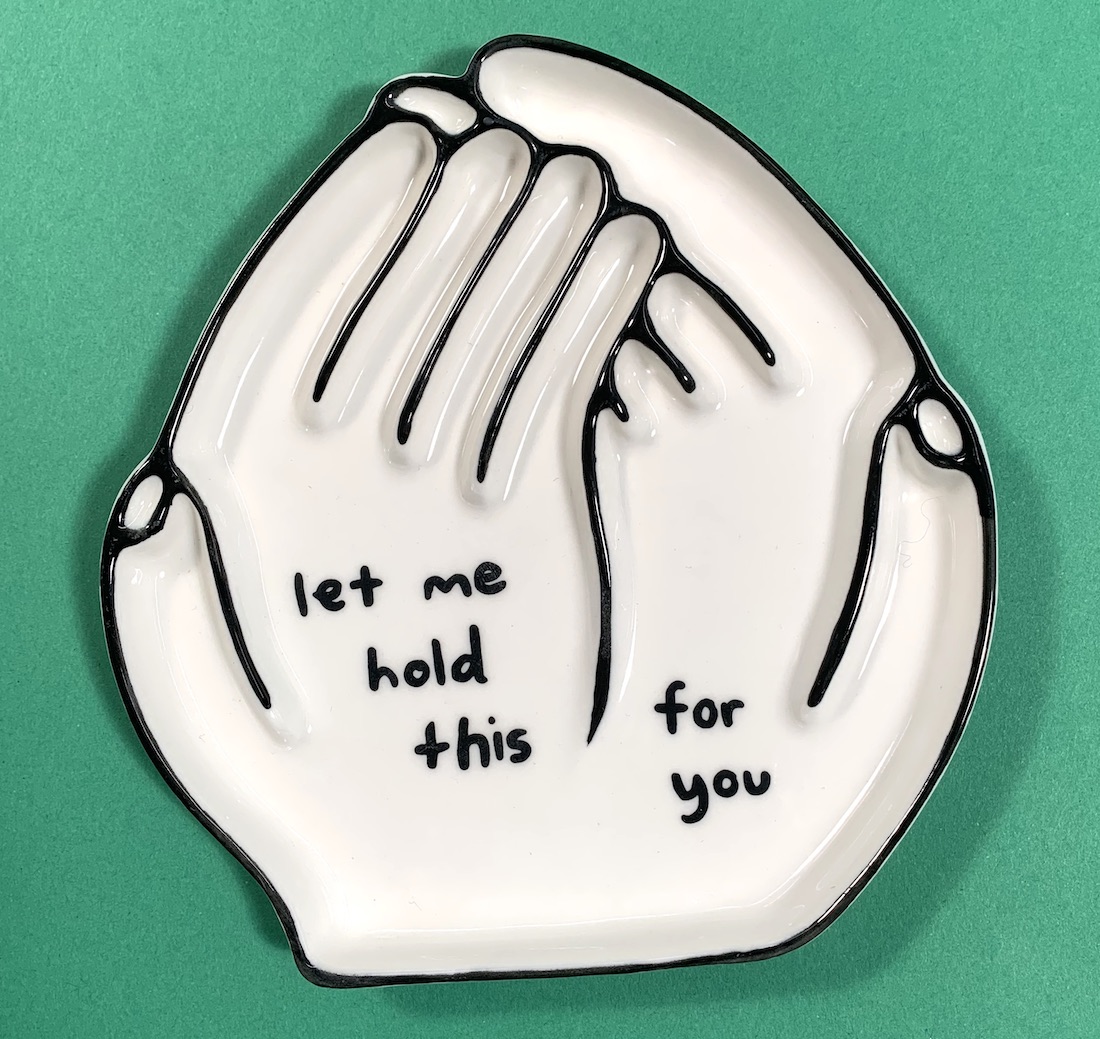 A ceramic tray in the shape of cupped hands with a message on the palms that reads "let me hold this for you"