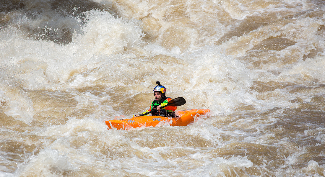 A man paddles a small boat amongst raging rapids.