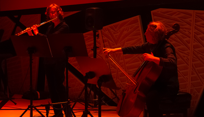 A violinist and cellist in Sonic Arts Ensemble play on a stage bathed in red light