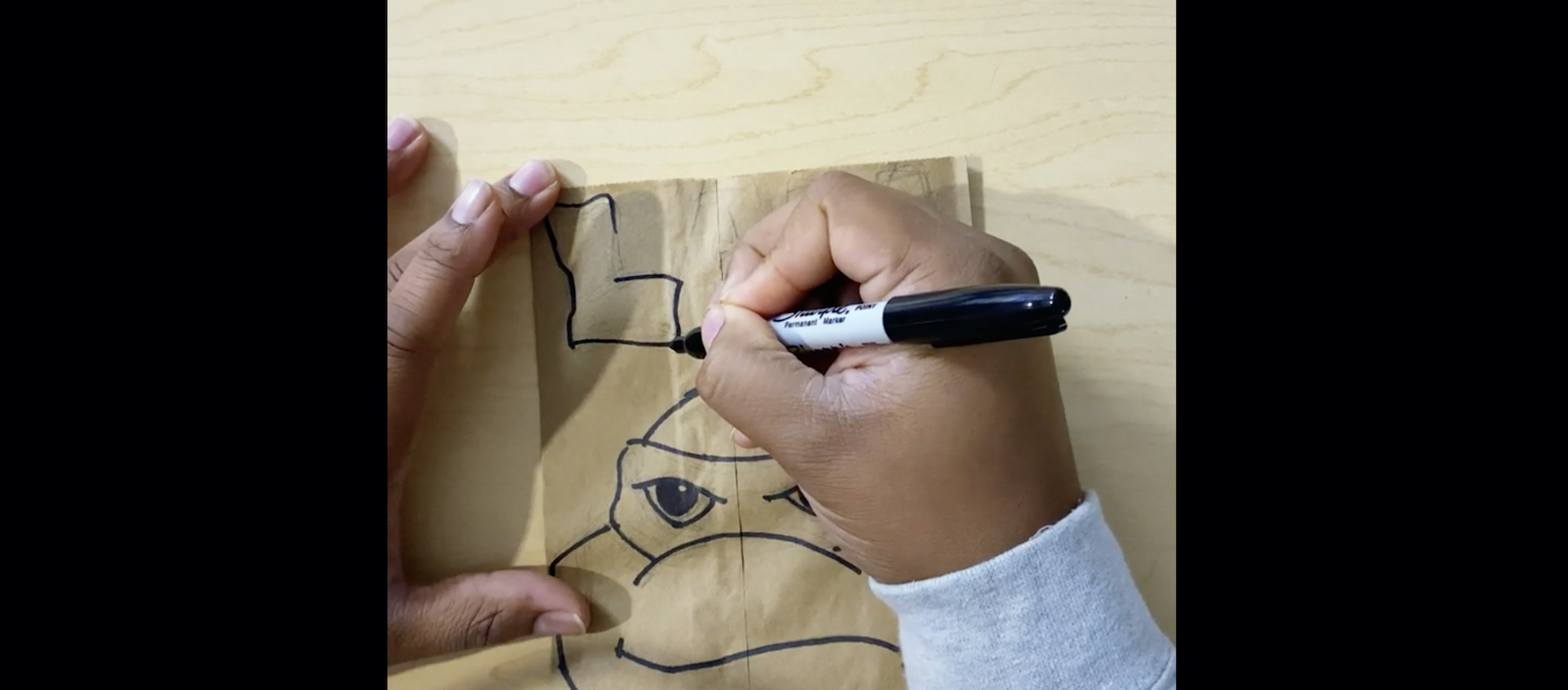 The hands of artist Alexander Chisley are seen drawing text with Sharpie marker above a drawing of a Teenage Mutant Ninja Turtle on a paper bag