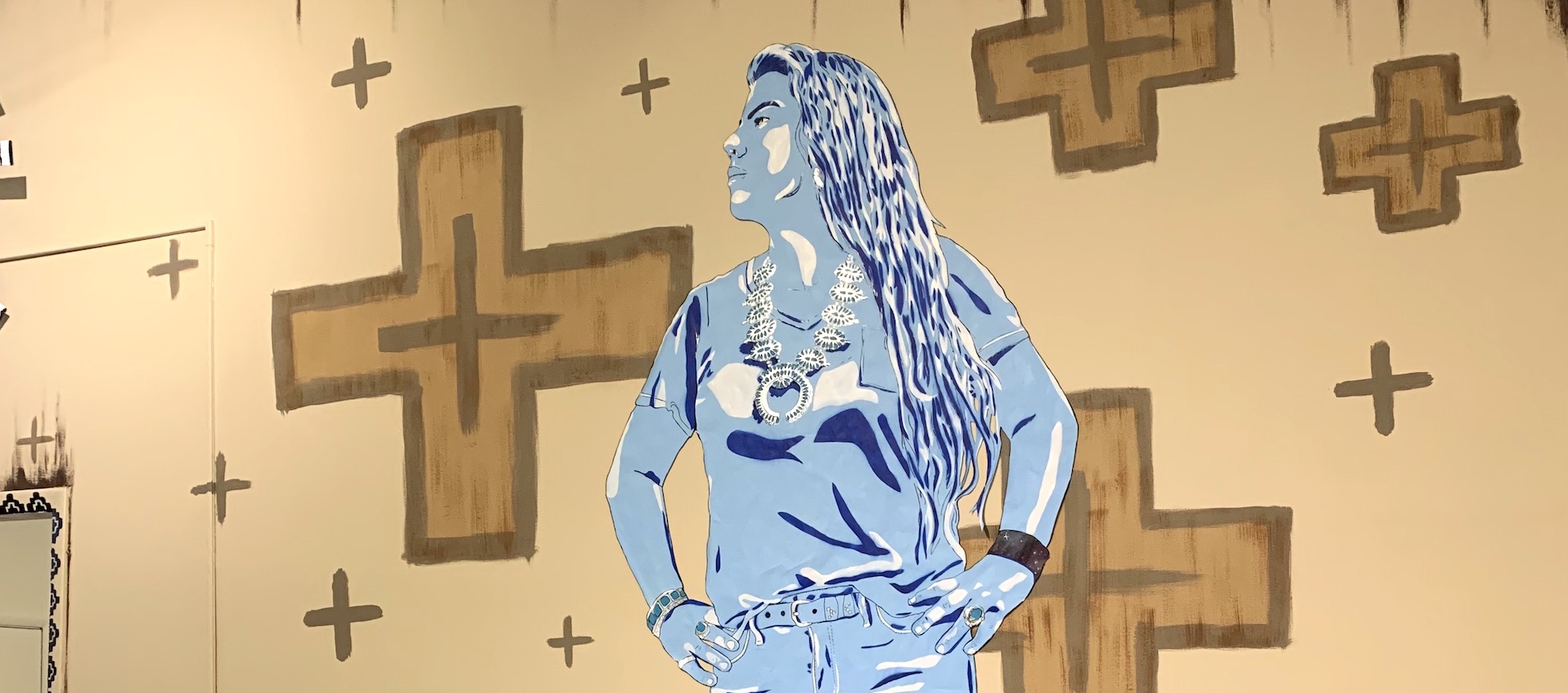 A stencil painted portrait of artist Olivia Barney by Stephanie Rond, wheat pasted onto a wall painted with an earth toned Native American motif on the wall of The Vanderelli Room