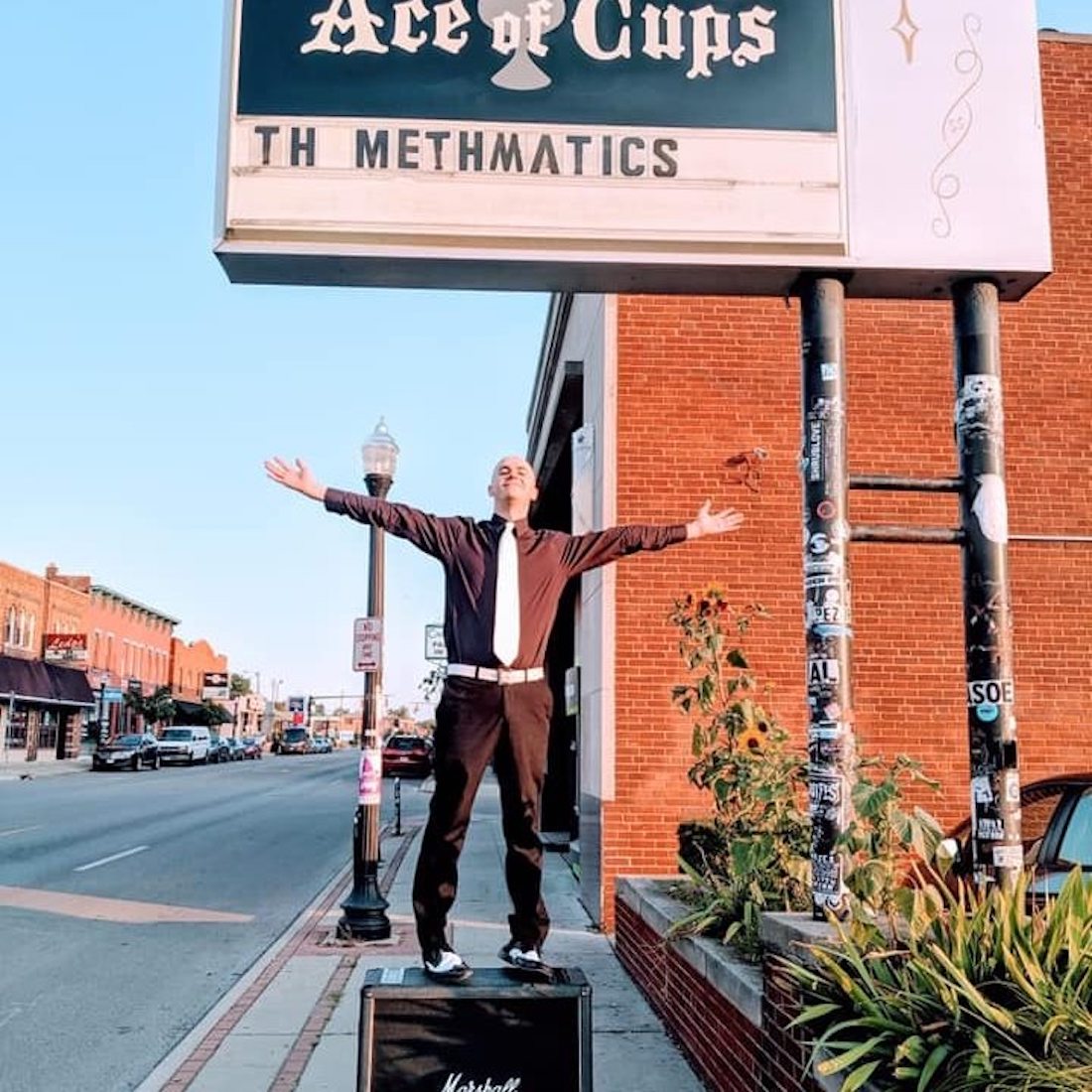 Joey Yates of the Columbus Ohio band Methmatics stands on top of his amplifier, arms outstretched, on North High Street beside the club Ace of Cups. Its marquee can be seen above him