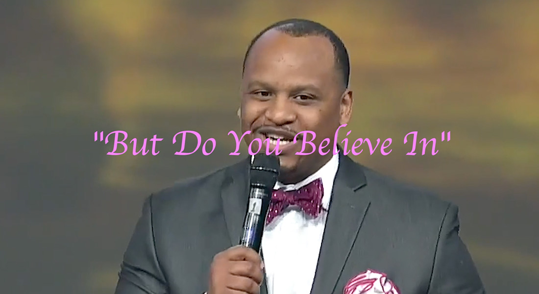 Image of a man with a moustache and microphone. He is wearing a bowtie and pink text is overlaid the image that says "But do you believe in."