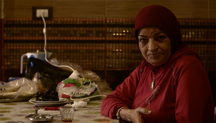 A elderly female in red hijab looking towards the camera.
