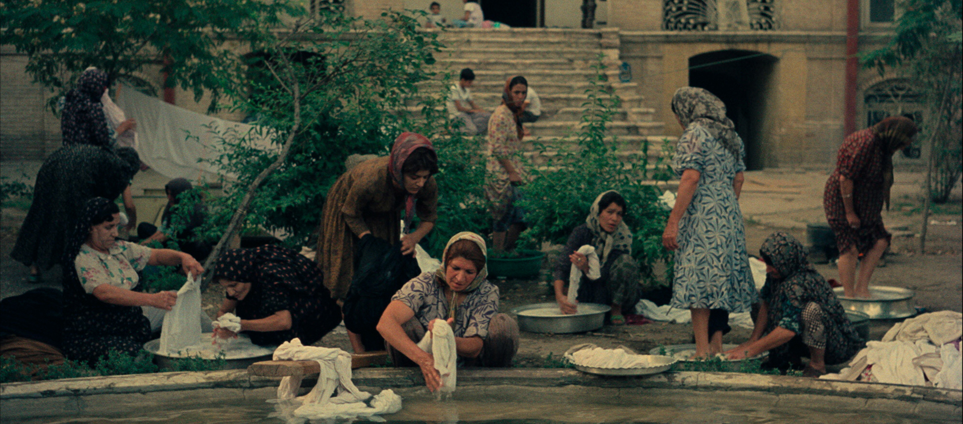 An image of several people in a town square standing around a fountain washing clothes and congregating