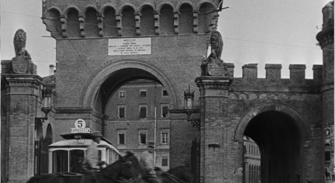A black and white image of two stone archways leading into a plaza. A trolley is driving into entrance