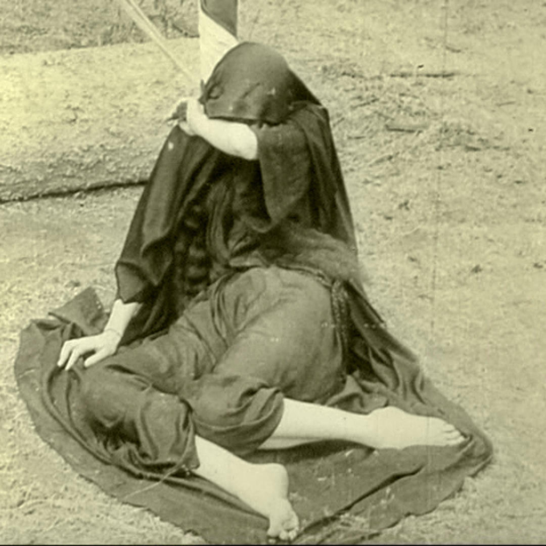 A woman sits in a long dress and shawl that covers her head, her arm covering her face, in a scene from Lois Weber's 1915 drama Hypocrites