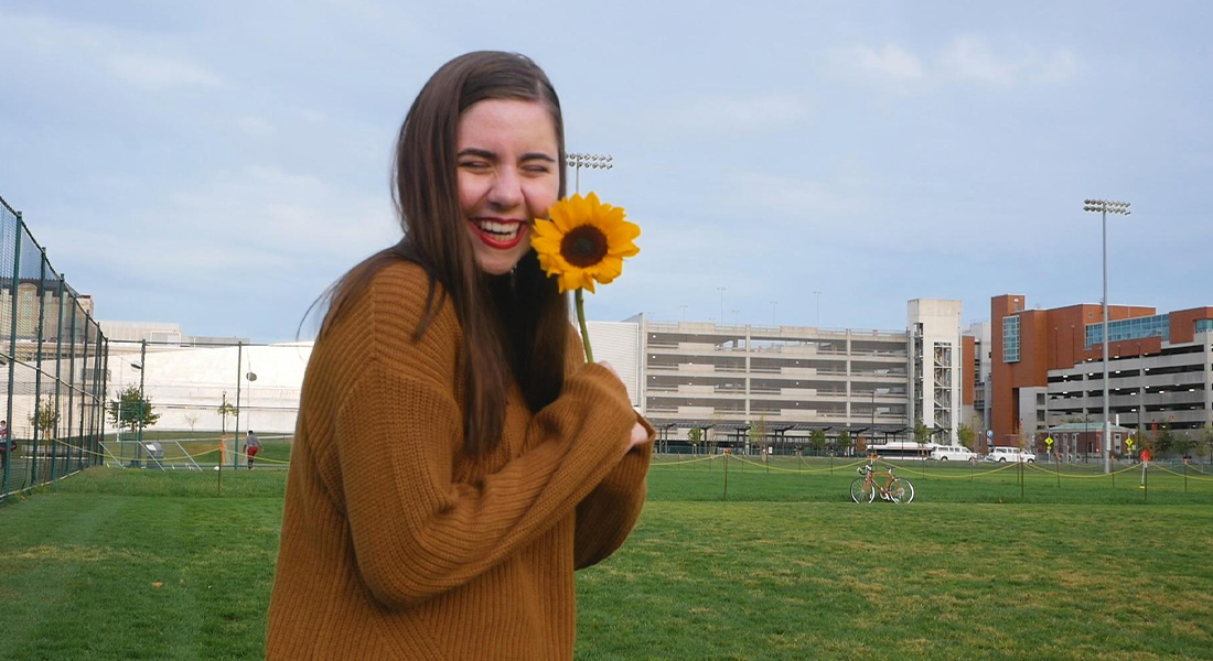 a young woman smiling with a sunflower in her hand.