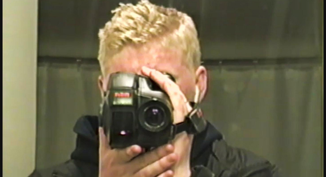 a blonde person looking through a camera.