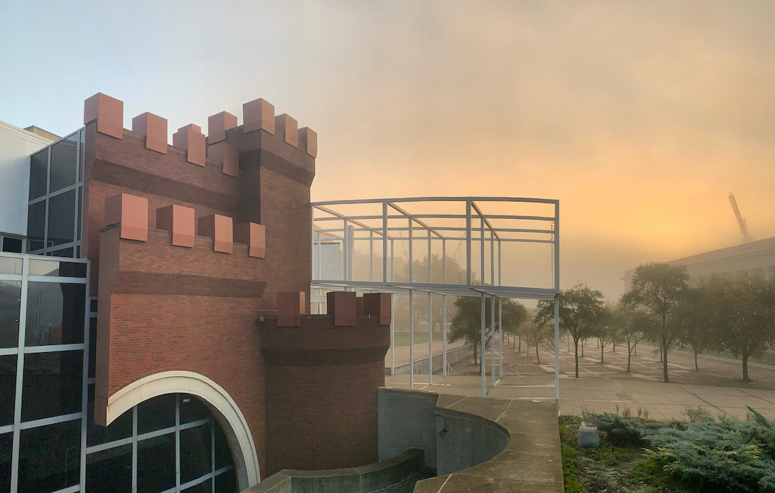 The Wexner Center for the Arts building with addition of Chris Burden's Wexner Castle to the exterior, seen in the foreground with a yellow sunrise sky and a construction crane seen in the background